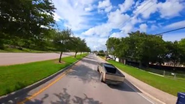 Tesla Cybertruck yerleşim bölgesindeki iki şeritli otoyoldan geçiyor. Modern aracı takip eden FPV insansız hava aracı görüntüleri.