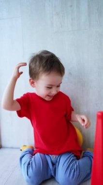 Güzel siyah saçlı erkek bebek kafasına bir piramit yüzük takıyor. Sevimli küçük çocuk evde neşeyle oynuyor. Dikey video.