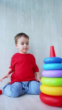 Büyüleyici beyaz bir erkek bebek piramit kuruyor. Odasında neşeli bir şekilde oynayan bebeğe düşük açılı bir bakış açısı. Dikey video.