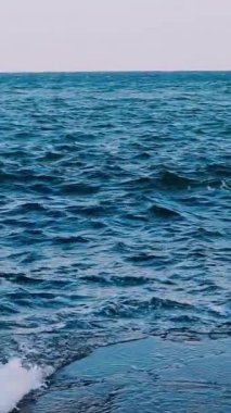 Dalgalar taş plajına çarpıyor. Deniz suyunun inanılmaz manzarası. Mavi su yüzeyi. Deniz suyunun güzel hareketi. Ağır çekim. Dikey video