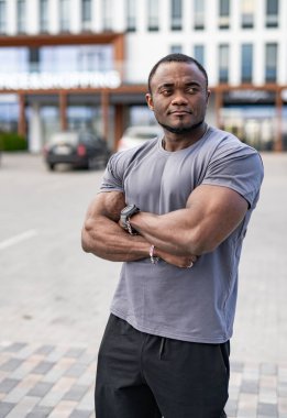 Şehir ortamında kendine güvenen güçlü bir adam. Kaslı bir adam şehir ortamında çapraz kollarla duruyor.