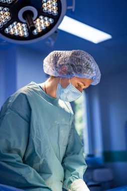 Tıbbi uzman ameliyathanede ameliyat yapıyor. Kendini adamış bir cerrah, iyi aydınlatılmış bir ameliyathanede cerrahi bir işlem sırasında dikkatle odaklanır.