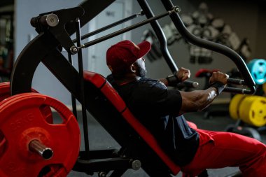 Yoğun kapalı spor salonları. Kırmızı elbiseli bir adam spor salonunda çekiş egzersizi yapıyor, özel ekipman kullanarak kuvvet eğitimine odaklanıyor..