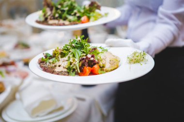 Baharda bir ziyafette taze salata servisi yapan garson. Bir garson canlı bir ziyafet sırasında iki tabak renkli salatayı, yeşillikleri, domatesleri ve süsleri nazikçe dengeler..