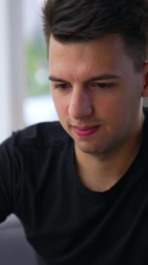 Dizüstü bilgisayarla uğraşan meşgul genç adam. Brunet erkek çalışanı ofis işine yoğunlaştı. Arkaplan bulanık. Dikey video