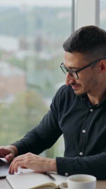 Laptop 'ta çalışan koyu saçlı serbest çalışan bir adam. Rahat adam iyi bir ruh hali içinde bilgisayarının başında çalışıyor. Arkaplan bulanık. Dikey video