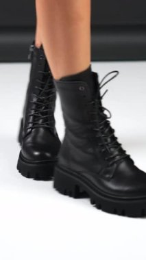 Çıplak kadın bacakları modern stil alçak çizmelerle yürür. Siyah ve beyaz arka planda bağcıkları olan deri siyah sonbahar çizmeleri. Dikey video