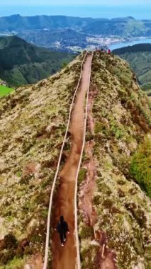 Dağın zirvesine çıkan yolda yürüyen bir kadın turisti takip etmek. Azorelar 'ın olağanüstü doğası üzerine hava perspektifi. Dikey video.