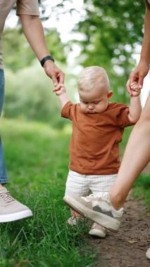 Anne ve babasını ellerinden tutan tatlı çocuk ayaklarına bakıyor. Sevimli çocuk da ayaklarını yere vurmaya başlıyor. Dikey video.