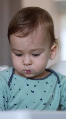 Bir yaşındaki erkek bebek bir beslenme sandalyesinde oturup kaşıkla yemek yiyor. Annesi tarafından kaşıkla beslenen sevimli beyaz çocuk. Kapat..