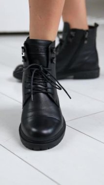 Çıplak bacaklı manken, bağcıklı siyah deri çizmeleri gösteriyor. Kadın, ayakkabı ayakkabısı için ayağa kalkar traktörün ayakkabı tabanına. Kapat..