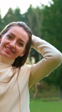 Sıcak beyaz kazaklı, gülümseyen beyaz kadın uzun saçlarına dokunup sallıyor. Sonbahar parkında dışarıda güzel vakit geçirmek..