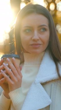 Elinde kağıt bardak tutan çekici esmer kadın var. Kadın sonbahar mevsiminde doğa yürüyüşü yapıyor..