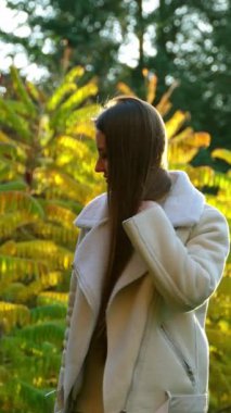 Parlak yapraklarla güzel çalılıklarda duran pozitif romantik kadın. Kameranın önünde uzun esmer saçlarını sallayan bir kadın. Sonbahar günü arkaplanı.