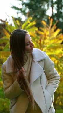 Güzel, genç bir kadın güneşin altında uzun, siyah saçlarını sallıyor. Bayan parkta harika bir sonbahar günü geçiriyor..