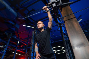 Geceleri modern bir spor salonunda halterci eğitimi. Çağdaş bir spor salonunda halter egzersizi yapan bir adam. Parlak ve renkli ışıklar altında güç gösterisi yapıyor..