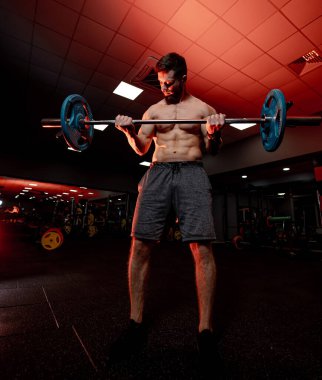 Adam loş spor salonunda halteri kaldırıyor. Kaslı bir adam halteri kaldırır, spor salonundaki antrenmanına odaklanır ve akşam saatlerinde ortam aydınlatmasıyla....