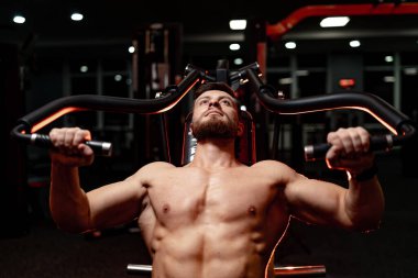 Adam geceleri loş ışıkla spor salonunda egzersiz yapıyor. Bir adam loş aydınlatılmış bir spor salonunda ağırlık kaldırır. Egzersiz yaparken gücünü gösterir ve odaklanır..