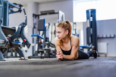 Genç bir kadın spor salonunda vücut egzersizi yapıyor. Genç bir kadın, gündüz vakti bir fitness merkezinde tahta egzersizleri yaparken karnını güçlendirmeye odaklanır..