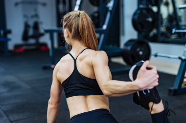Spor salonunda esneme hareketleri yapan genç bir kadın. Bir kadın, vücudunu yoğun bir idmana hazırlamak için spor salonunda esneme egzersizi yapıyor.