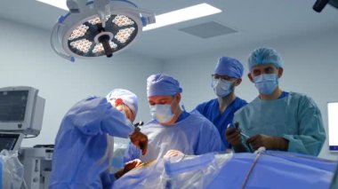 Asistan cerrahi aletleri baş cerraha veriyor. Beyin cerrahı yuvarlak lamba altında ameliyat yapıyor.