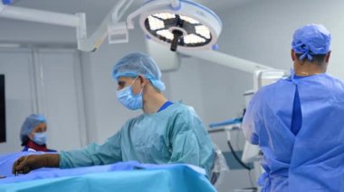 Erkek ameliyat hemşiresi metal forseps kullanarak sünger alıyor. Sıhhiye cerrahlara malzeme dağıtır..