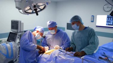 Erkek baş cerrah cerrahi bir alet kullanarak çok çaba sarf ediyor. Doktor bir hemşireye kullanılmış bir enstrüman verir ve bir tane daha alır..