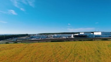 Sarı alanın üzerinden uçarak büyük bir endüstriyel fabrikanın arazisine yaklaşıyorlar. Arkaplanda mavi gökyüzü.