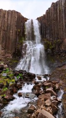 Resimli sütun kayalıklarından düşen güzel bir su manzarasına yaklaşıyoruz. İzlanda 'nın görkemli ve gerçekçi olmayan doğası. Dikey video.