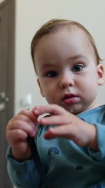 Mavi tişörtlü bebek elinde ayakkabı bağcığına merakla bakıyor. Şirin çocuk neşeli bir şekilde sallayan bir iple oynuyor. Düşük açı yakın çekim. Dikey video