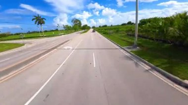 Yeşillik çimenlik boyunca asfalt otobanından geçen Tesla Cybertruck 'ı takip ediyoruz. FPV insansız hava aracı güneşli bir günde kırsal alanda gelecekteki arabaya yetişiyor..