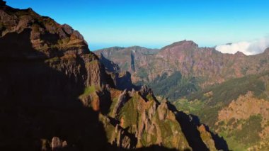 Keskin tepeleri olan muhteşem dağlar. Güneş kayaların yamaçlarını aydınlatıyor. Arkaplanda gök mavisi.