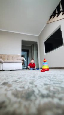 Mutlu erkek bebek evde oynuyor. Neşeli çocuk yerde sürünerek kameraya doğru yaklaşıyor. Dikey video.