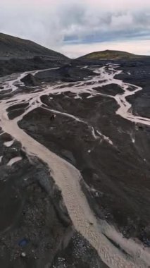 Dar nehirler ağı kayalık vadiyi geçer. Turistler İzlanda 'nın çorak arazileri arasında dururlar. Üst Manzara. Dikey video.