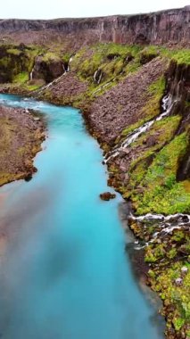 Dağların eteklerinden akan masmavi bir nehrin su üzerinde uçmak. Kayalardan çok sayıda küçük şelale düşüyor. Dikey video.