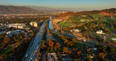 Günbatımı Los Angeles, Kaliforniya, ABD 'de. Canlı otoyol ve Los Angeles nehri üzerindeki insansız hava aracı görüntüleri. Arkaplanda dağlar.