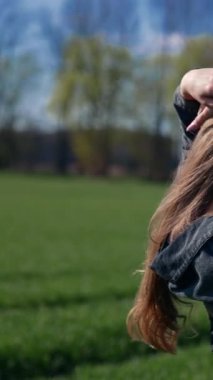 Kırsal kesimde güzel bir kız. Sahada poz veren uzun sarı saçlı çekici genç bir manken. Yörünge görüntüsü. Dikey video