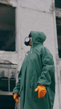 Gaz maskesi takan ve açık havada güvenlik kıyafeti giyen biri. Kıyametin eşiğinde duran, solunum cihazı ve koruyucu üniforma giyen bir adam. Kimyasal saldırı. Dikey video