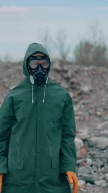 Güvenlik kıyafeti giymiş bir adam ve çöp arka planında solunum cihazı var. Radyoaktif bölgede terk edilmiş bir yerde koruyucu kostümlü ve gaz maskeli çılgın adam dans ediyor. Dikey video