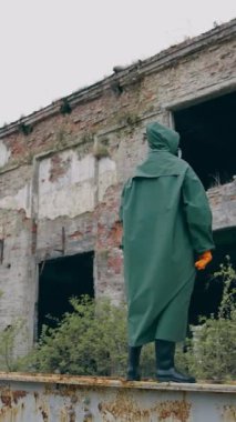 Terk edilmiş yerde koruyucu elbiseli bir adam. Güvenlik kıyafetli adam yıkılmış binaların arkasında tek başına duruyor. İnsan yok. Kıyamet konsepti. Dikey video