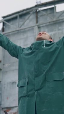 Kurtulan kişi yıkılmış yerde derin bir nefes alıyor. Koruyucu giysili bir adam elinde gaz maskesi tutarken yıkık binanın arka planında temiz havanın tadını çıkarıyor. Dikey video