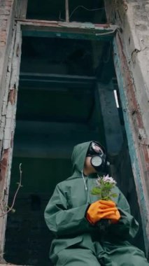 Elinde çiçek tutan gaz maskeli bir adam. Terk edilmiş binada çiçekli, güvenlik kıyafetli biri oturuyor. Ekoloji kirliliği kavramı. Kimyasal saldırı sonucu. Dikey video