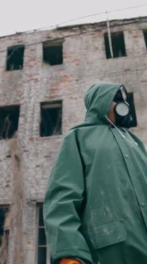 Şehirdeki kimyasal saldırının sonuçları. Güvenlik kıyafetli ve maskeli bir insan penceresiz yıkılmış binanın arka planında tek başına nefes alıyor. Dikey video