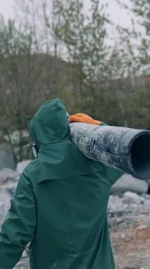 Güvenli giysili bir adam tehlikeli bölgede yürüyor. Koruyucu üniformalı ve solunum cihazlı insanlar kirli havayla dolu terk edilmiş bir yerde boru taşıyorlar. Dikiz aynası. Dikey video