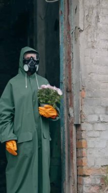 Kıyamet sonrası mekanında bir kişi var. Koruyucu giysili bir adam, ekolojik felaketten sonra terk edilmiş bir yerde çiçeklerle. Radyasyon emisyonu. Dikey video