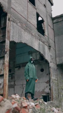 Mahvolmuş yerde takım elbiseli bir kurtulan. Gaz maskeli ve koruyucu giysili bir adam terk edilmiş bir yerde tek başına duruyor. Kıyamet sonrası konsepti. Dikey video