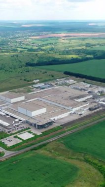 Yeşil arazideki fabrika. Yeşil tarlalar ve ormanlarla çevrili büyük sanayi bölgesi. Doğada üretim. Hava görüntüsü. Dikey video