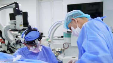 Cerrahi lensler takan erkek cerrah ameliyatta. Doktora yardım etmek ameliyat masasının üzerinde duruyor..