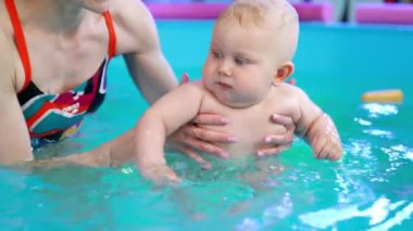 Kafkas antrenörü bebeği havuzda sağa sola hareket ettiriyor. Pozitif koç bir çocuğa yüzmeyi öğretiyor..
