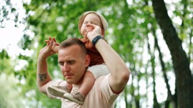 Kafkasyalı pozitif bir adam, omzunda bir keple bir bebek tutuyor. Baba oğlunu elinden tutup parkta koşar..